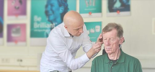 Ein Fachmann der das Hörgerät eines älteren Manns anpasst