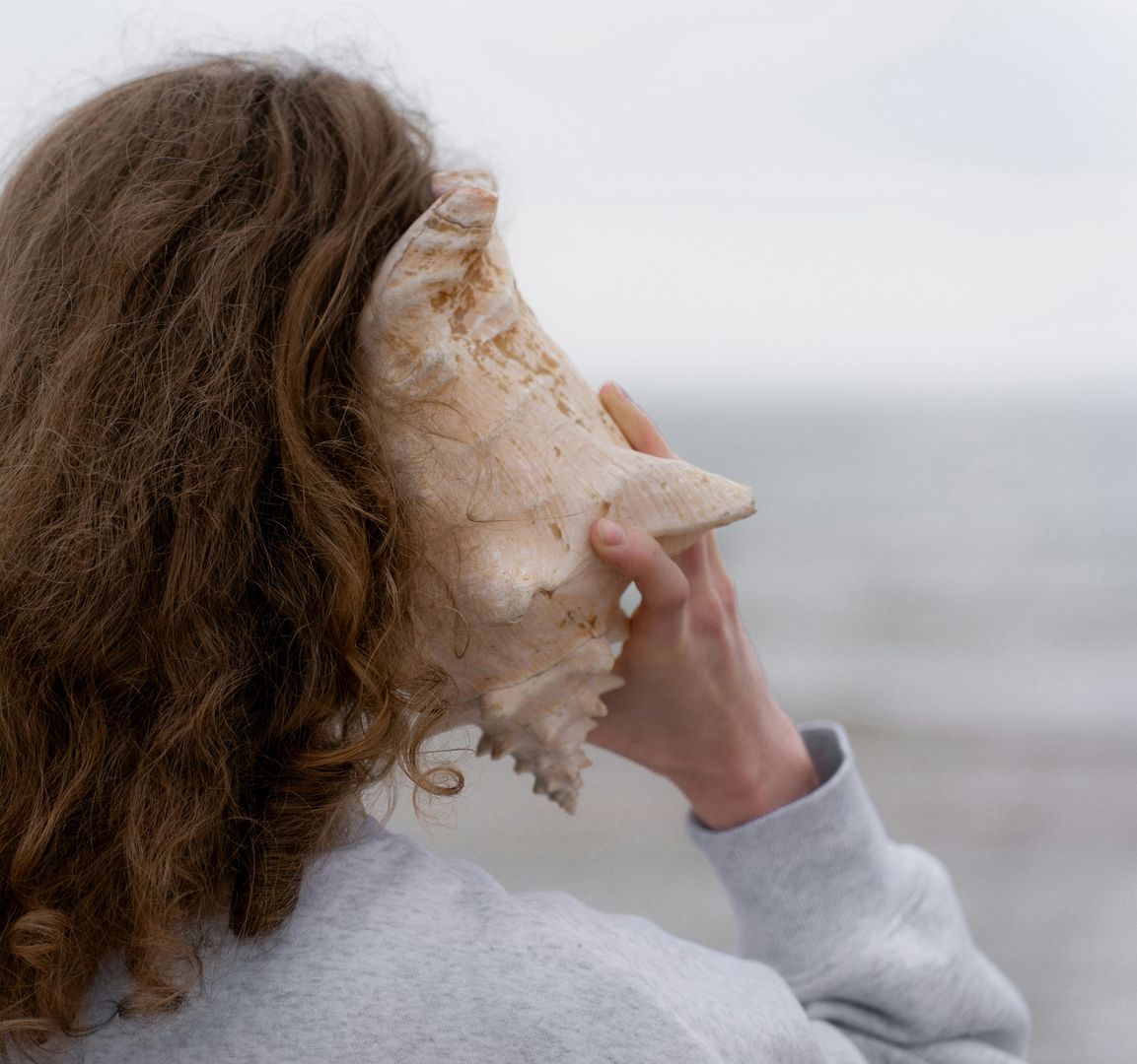 Eine Frau von hinten die eine Muschel an Ihr Ohr hält